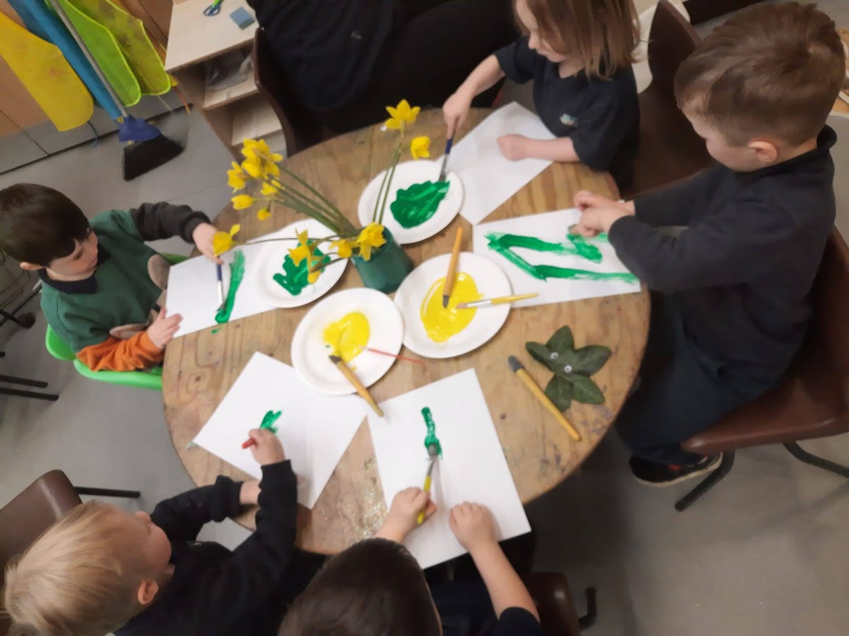 Group of young children sat around a table painting pictures of daffodils